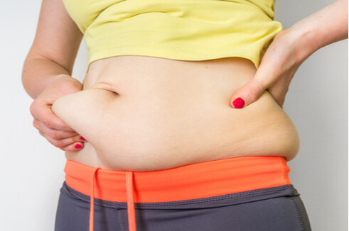 Woman grabbing fat and skin on her abdomen that could benefit from tummy tuck surgery.