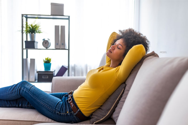 Woman lounging on couch with her arms behind her head. 