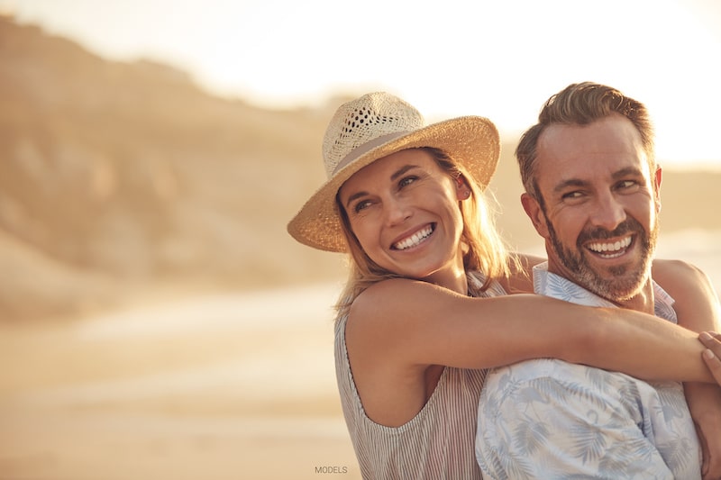 Attractive middle-aged couple smiling and holding each other on the beach.